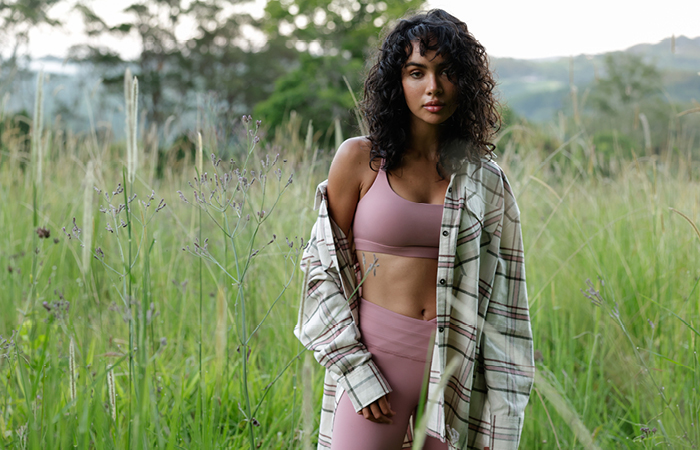 a woman wearing dusty pink leggings, pink sports bra and pink and white check button up shirt